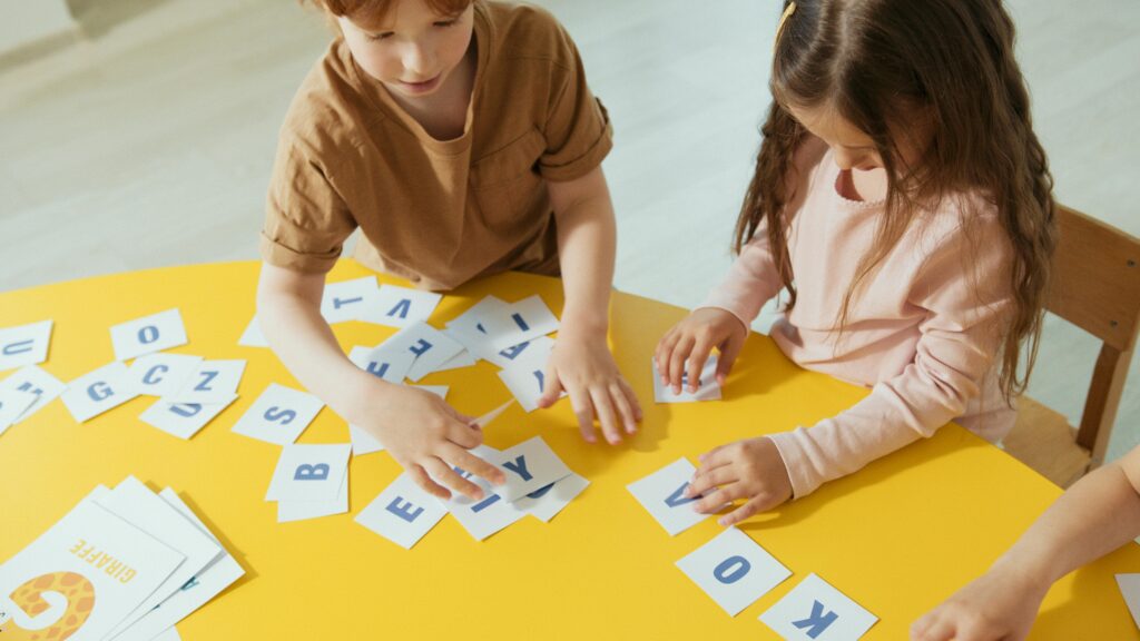 Two children interacting with alphabet cards at a yellow table, enhancing learning and creativity.
