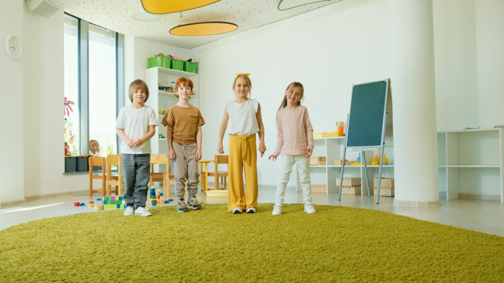 Four cheerful children standing in a well-lit classroom with playful decor.