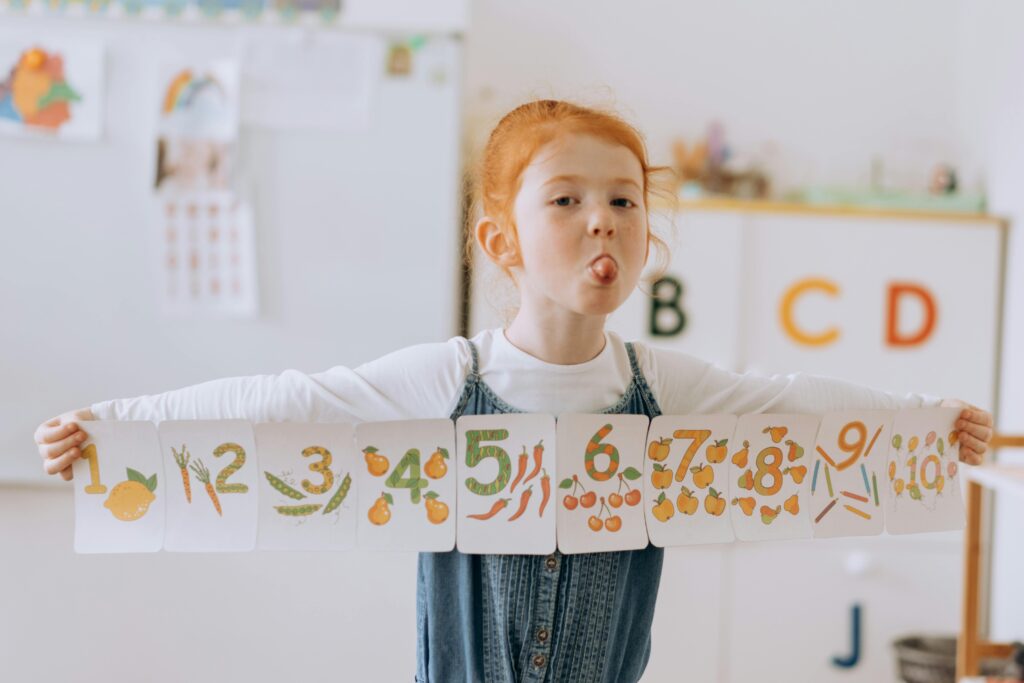 Happy redhead child holding number cards in a classroom, enjoying fun learning.